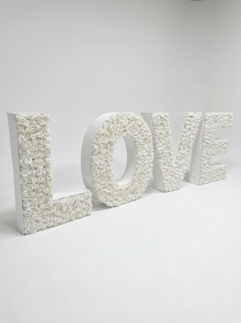 Grandes lettres "LOVE" blanches décorées de fleurs, posées au sol pour décoration d’événement