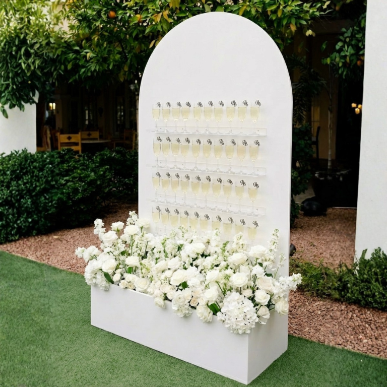 Mur à champagne blanc avec verres et fleurs en bas, utilisé pour réception événement